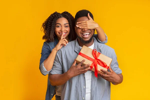 Loving black woman covering her boyfriends eyes and giving him gift — Stock Photo, Image