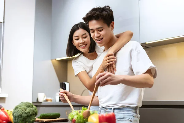 Asiática novia abrazando novio cocina ensalada para la cena en casa — Foto de Stock