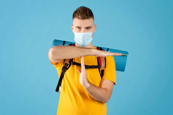 Reisverbod tijdens virale epidemie. Cool millennial man met rugzak dragen masker en gebaren STOP op blauwe achtergrond — Stockfoto