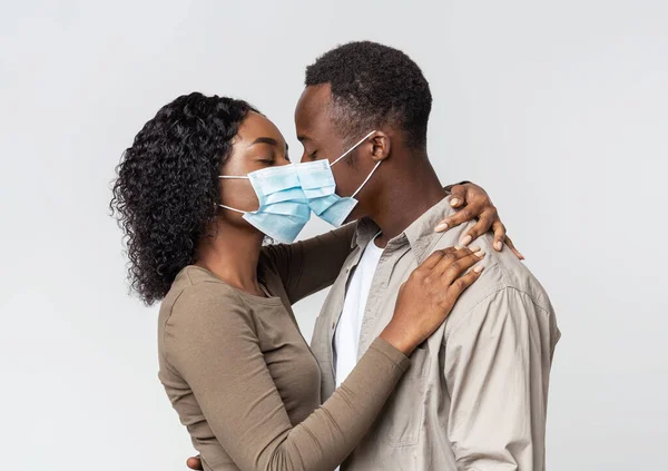 Romantic african couple in face masks kissing over grey