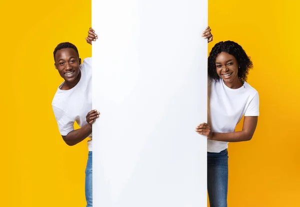 Vrolijk Afrikaans paar houden leeg bord voor reclame — Stockfoto