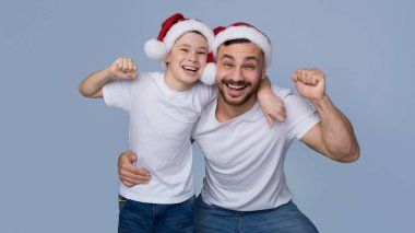 Noel Baba şapkalı neşeli oğul ve baba kamerada tezahürat yapıyor.