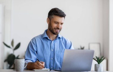 Milenyum erkek girişimcisi dizüstü bilgisayar kullanıyor ve işyerinde notlar alıyor.