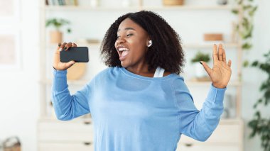 Akıllı telefonu mikrofon olarak kullanıp şarkı söyleyen siyah kadın.