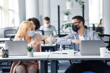 Tecritten sonra modern beşlik iş başında ve yeni normaller. Mutlu bin yıllık koruyucu maskeli kadın ve erkek iş yerinde dirseklerine dokunur.