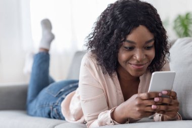 Gülümseyen Afrikalı kadın akıllı telefonuyla evde vakit geçiriyor, arkadaşlarıyla mesajlaşıyor.