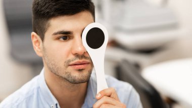 Serious male patient doing eye test in clinic clipart