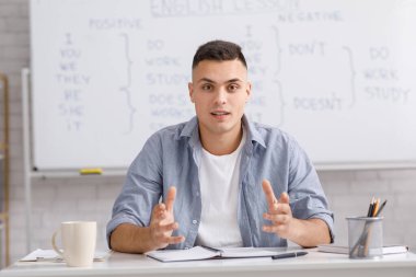 Evde koronavirüs salgını sırasında uzaktan çalışma, dersler ve çevrimiçi eğitim. Yakışıklı genç adam İngilizce kurallarını açıklıyor. Oturma odasında oturuyor.