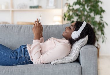 Rahatlamış bir hafta sonu. Telsiz kulaklıklı mutlu siyah kadın akıllı telefondan müzik dinliyor.