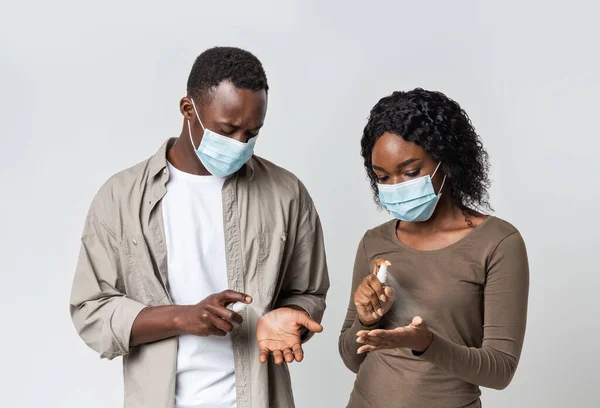 Young couple in face masks disinfect their hands with antiseptic