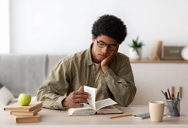 Aburrido adolescente afroamericano leyendo libro de texto, preparándose para un examen complicado en casa — Foto de Stock