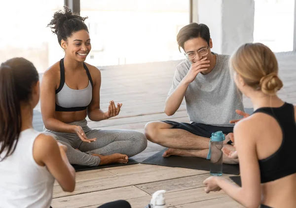 Sport multiculturale uomini e donne seduti su stuoie, chiacchierando dopo la lezione di yoga — Foto Stock