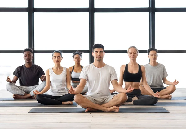 Meditación en grupo. Jóvenes hombres y mujeres multiétnicos meditando juntos en posición de loto — Foto de Stock