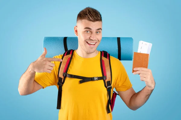 Positivo millennial chico con mochila apuntando a pasaporte internacional y billetes de avión en fondo azul estudio — Foto de Stock