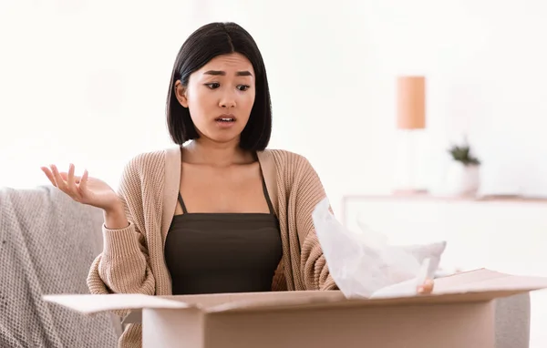 Frustrated young lady unpacking wrong parcel, delivery mistake