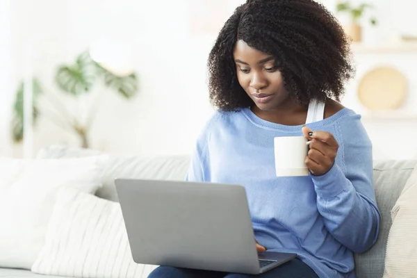 Mulher negra usando laptop e segurando xícara de café — Fotografia de Stock