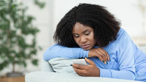 Разочарованная леди проверяет мобильный телефон сидя на диване — стоковое фото