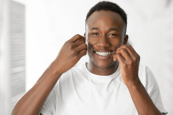 Feliz Afro-Americano Hombre Flossing dientes de pie en baño moderno —  Fotos de Stock