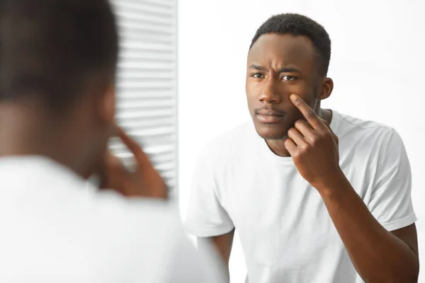 Preocupado preto cara tocando acne na cara em pé no banheiro — Fotografia de Stock