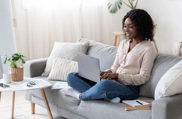 Gioiosa donna freelancer nera che lavora con il computer portatile a casa — Foto Stock