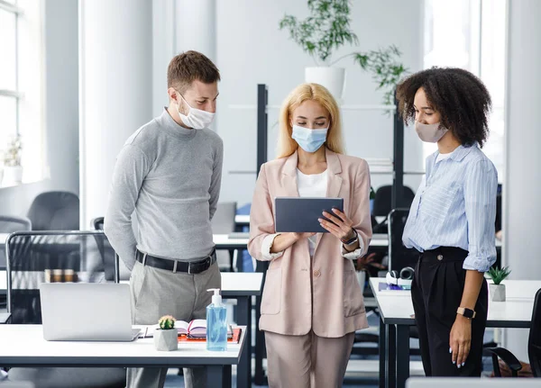 Nueva tarea, distanciamiento social y trabajo de oficina después del cierre. Joven mujer de negocios con máscara protectora da tareas a hombre europeo y señora afroamericana en el interior de la oficina — Foto de Stock