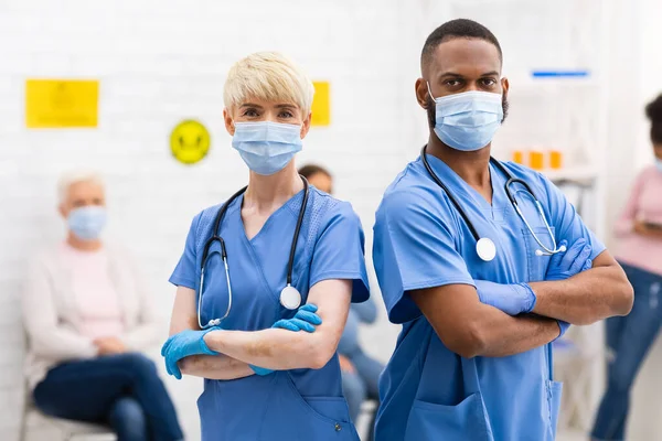 Dois médicos diferentes em máscaras médicas posando em pé no hospital — Fotografia de Stock