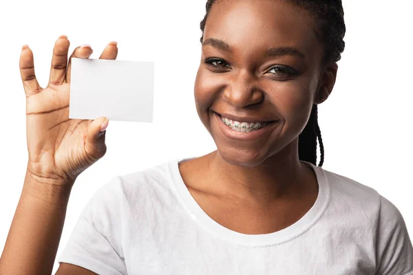 Czarna kobieta w aparacie pokazuje pustą wizytówkę, białe tło — Zdjęcie stockowe