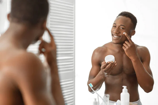 Preto cara aplicando creme no rosto pé sem camisa no banheiro — Fotografia de Stock