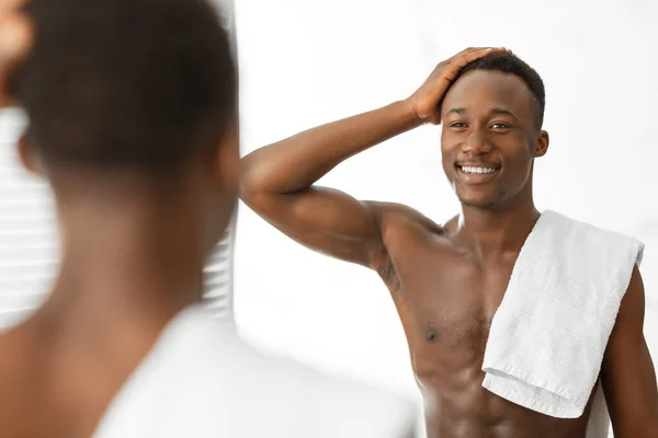 Negro hombre tocando pelo buscando en espejo de pie en cuarto de baño — Foto de Stock