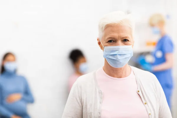 Señora mayor infectada con Coronavirus de pie usando máscara en el hospital — Foto de Stock