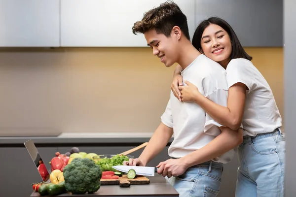 Asian Wife Hugging Husband While He Cooking Dinner In Kitchen — Stock Photo, Image