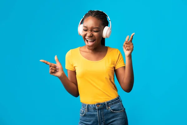 Millennial mujer negra escuchando música usando auriculares sobre fondo azul — Foto de Stock