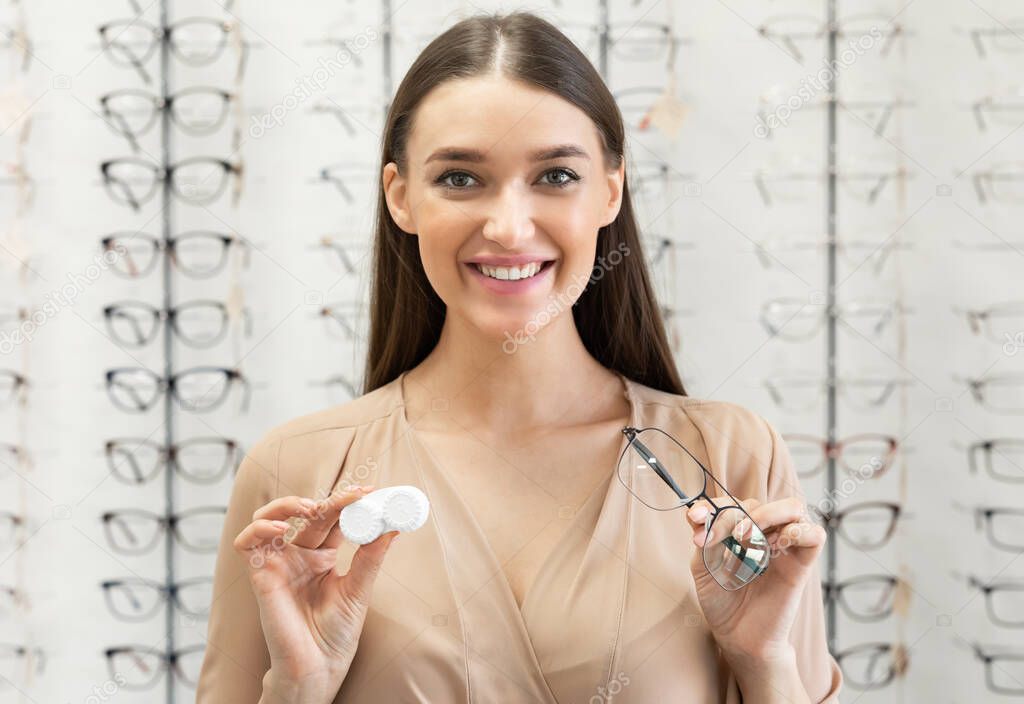 Smiling woman showing to camera eyeglasses and contacts