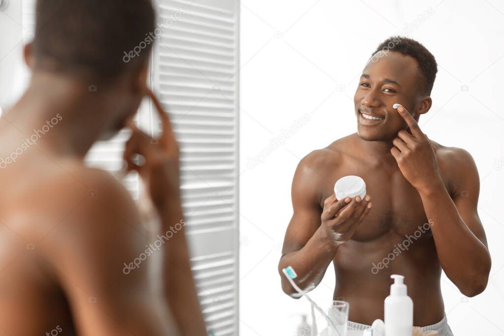 Black Guy Applying Cream On Face Standing Shirtless In Bathroom