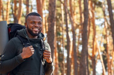 Sırt çantalı Afrikalı bir adam ormanda yürüyüş yapıyor.