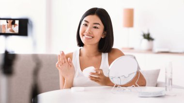 Genç bir kadın video bloğu için yüzüne krem sürüyor.