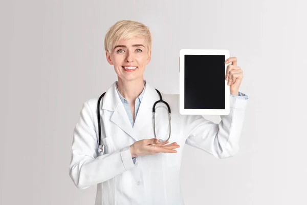 Dispositivo per lavorare con protezione della salute in clinica. Sorridente mostra signora adulta con mano sul tablet con schermo bianco — Foto Stock