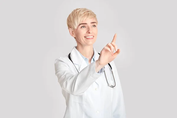 Medicina moderna, diagnóstico y ciencia. Sonriente doctora adulta presiona los dedos un espacio vacío para botón virtual —  Fotos de Stock