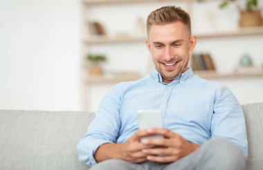 Evinde akıllı telefon kullanan gülümseyen adamın yakın çekimi.