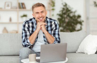 Genç adam kanepede oturuyor ve kameraya bakıyor.