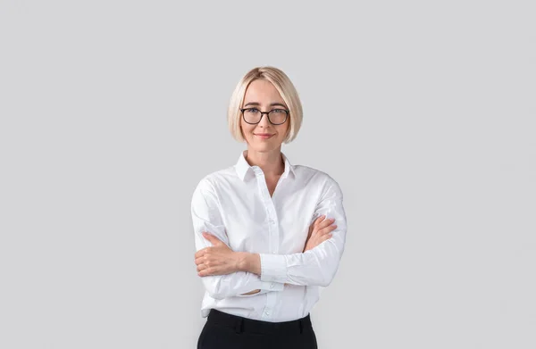 Femme d'affaires positive en tenue formelle et lunettes debout avec les bras croisés sur fond studio gris clair — Photo