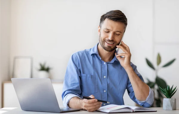 Sorridente uomo d'affari Prendere appunti pur avendo conversazione telefonica in ufficio — Foto Stock