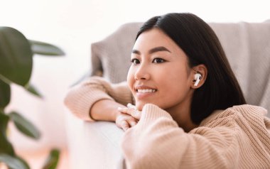 Kablosuz kulaklık takan Asyalı bir kadın müzik dinliyor.