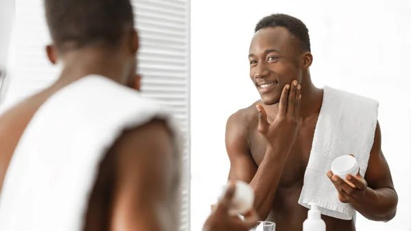 顔の保湿クリームを使用した黒男はバスルームで恥ずかしがり屋立って — ストック写真