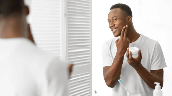 Africano hombre usando facial crema cuidado para la piel en cuarto de baño — Foto de Stock