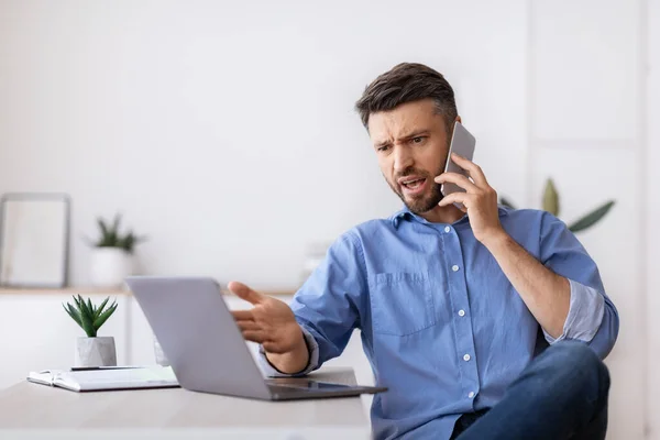 Boze zakenman in gesprek op mobiele telefoon en op zoek naar laptop scherm in kantoor — Stockfoto