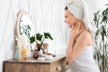 Güzel genç bir kadın tenine dokunuyor, aynaya bakıyor.