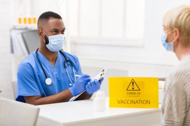 Doktor, Kapalı alan 19 aşısı randevusu sırasında hastayla konuşuyor.