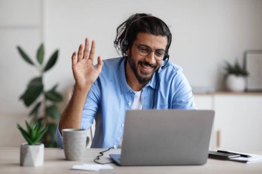 Uzaktan iletişim. Kulaklıklı Mutlu Batılı Adam Laptop Kamerasında El Sallıyor