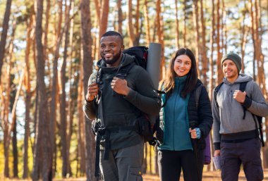Sonbahar ormanlarında yürüyüş yapan üç uluslararası arkadaş.